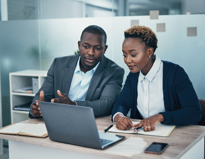 Two colleagues in a small office discussing work over a laptop